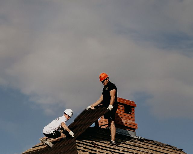 Roof repair crew at work Two roofers in safety helmets repairing a home roof on a cloudy day