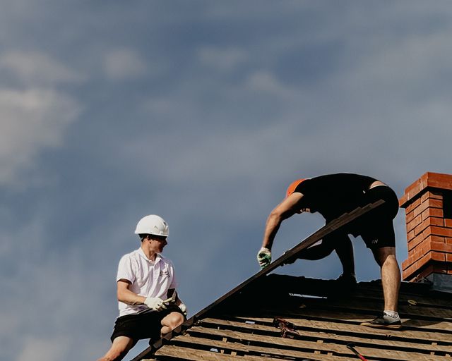 Roof repair crew at work Two roofers repairing a sloped home roof under a clear blue sky
