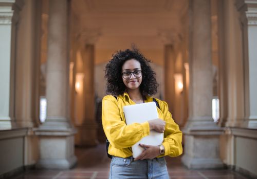 Free Confident woman in glasses standing with a laptop in an elegant indoor setting. Stock Photo