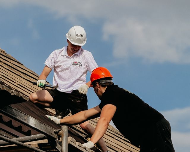 Roofers repairing a rooftop Two roofers in helmets repairing a rooftop under a clear sky