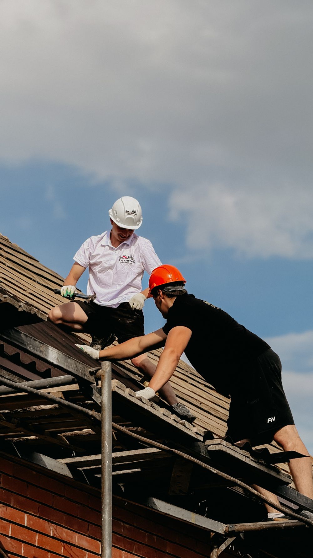 Roofers repairing a pitched rooftop under clear sky