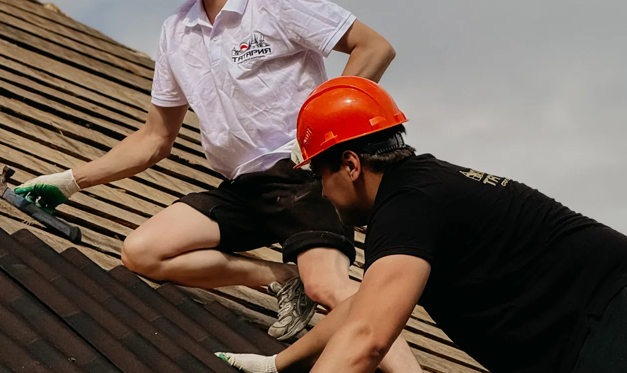 Construction workers repairing a residential roof with safety gear