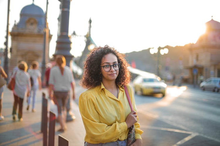 Woman In Yellow Button Up Shirt And Blue Jeans Walking Down Side Street