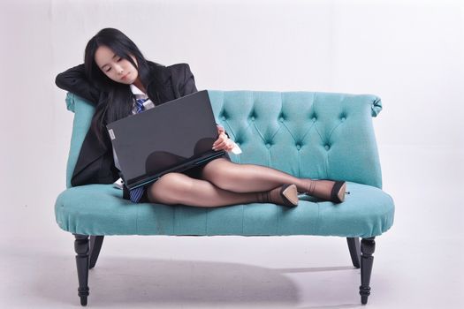 Businesswoman in formal attire reclining with a laptop on a teal sofa, indoors.