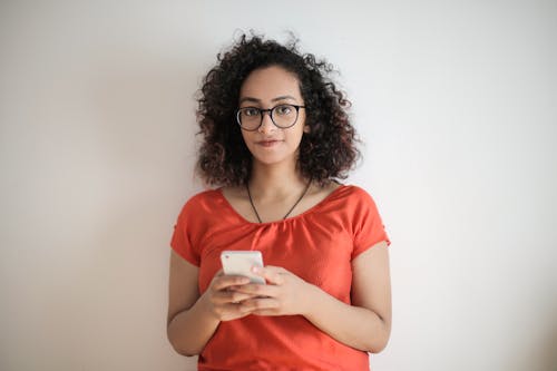 Free Photo of Woman in Red Top and Black Framed Eyeglasses Holding a White Smartphone Stock Photo