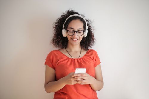 Free Smiling woman with curly hair in headphones using a smartphone against a white background. Stock Photo