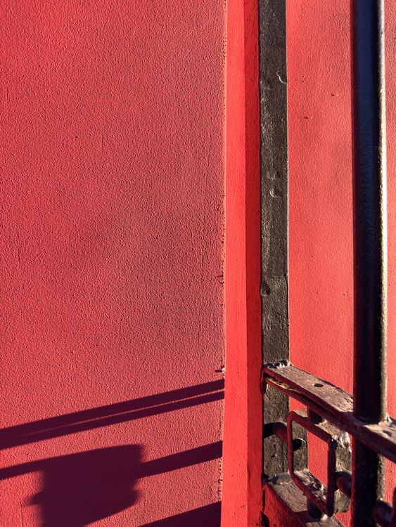Red Railing Texture Red Wall with Black Iron Railings in Sunlight · Free Stock Photo
