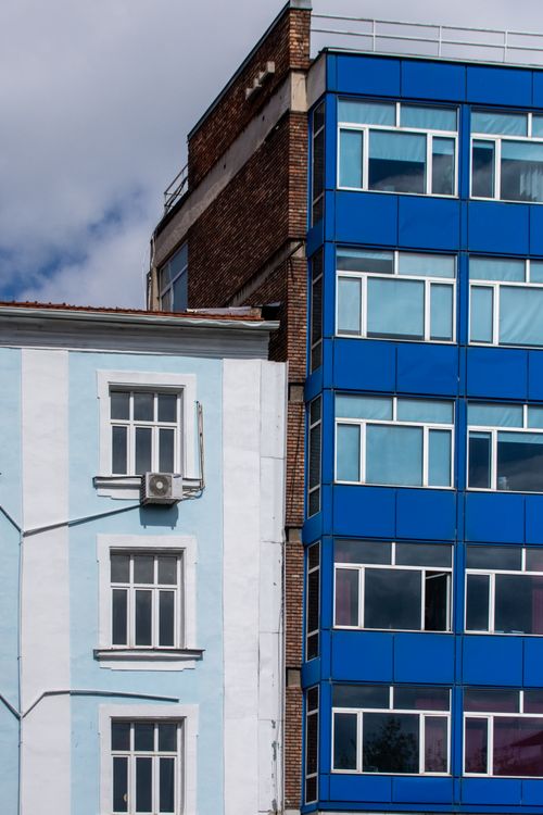 Free A striking juxtaposition of modern blue and vintage white building facades under a clear sky. Stock Photo