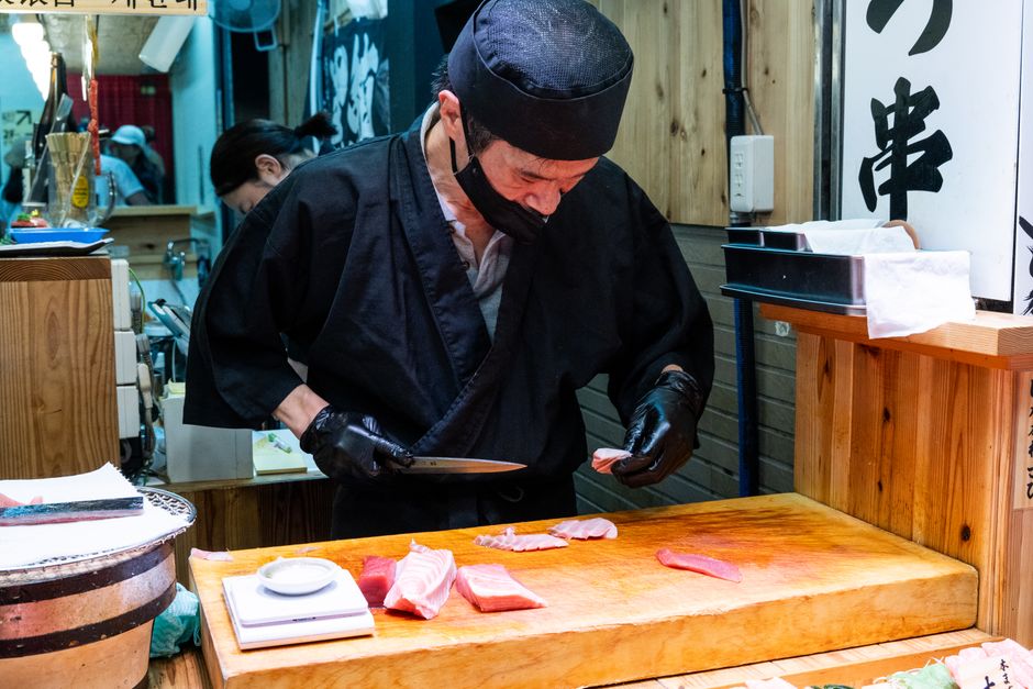 Sushi chef carefully slicing fresh fish behind a wooden sushi bar