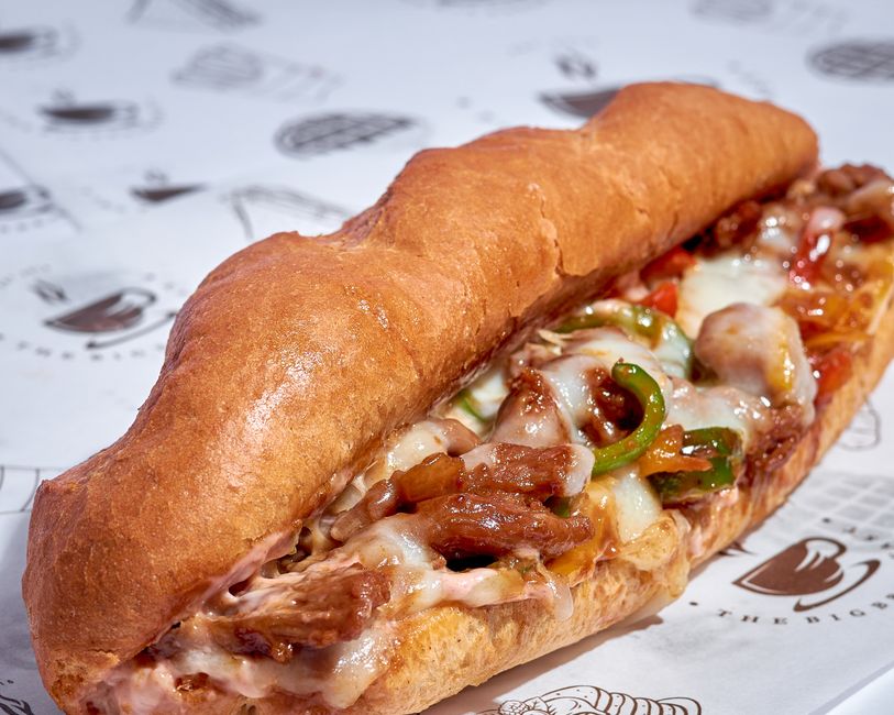 A halved Italian sub roll piled with folded slices of salami, capicola, and provolone, topped with shredded lettuce, tomato, red onion, and a drizzle of oil and vinegar.