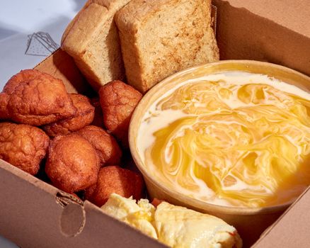 A cardboard box filled with Akara, pap, bread, and egg, showcasing a classic Nigerian breakfast.