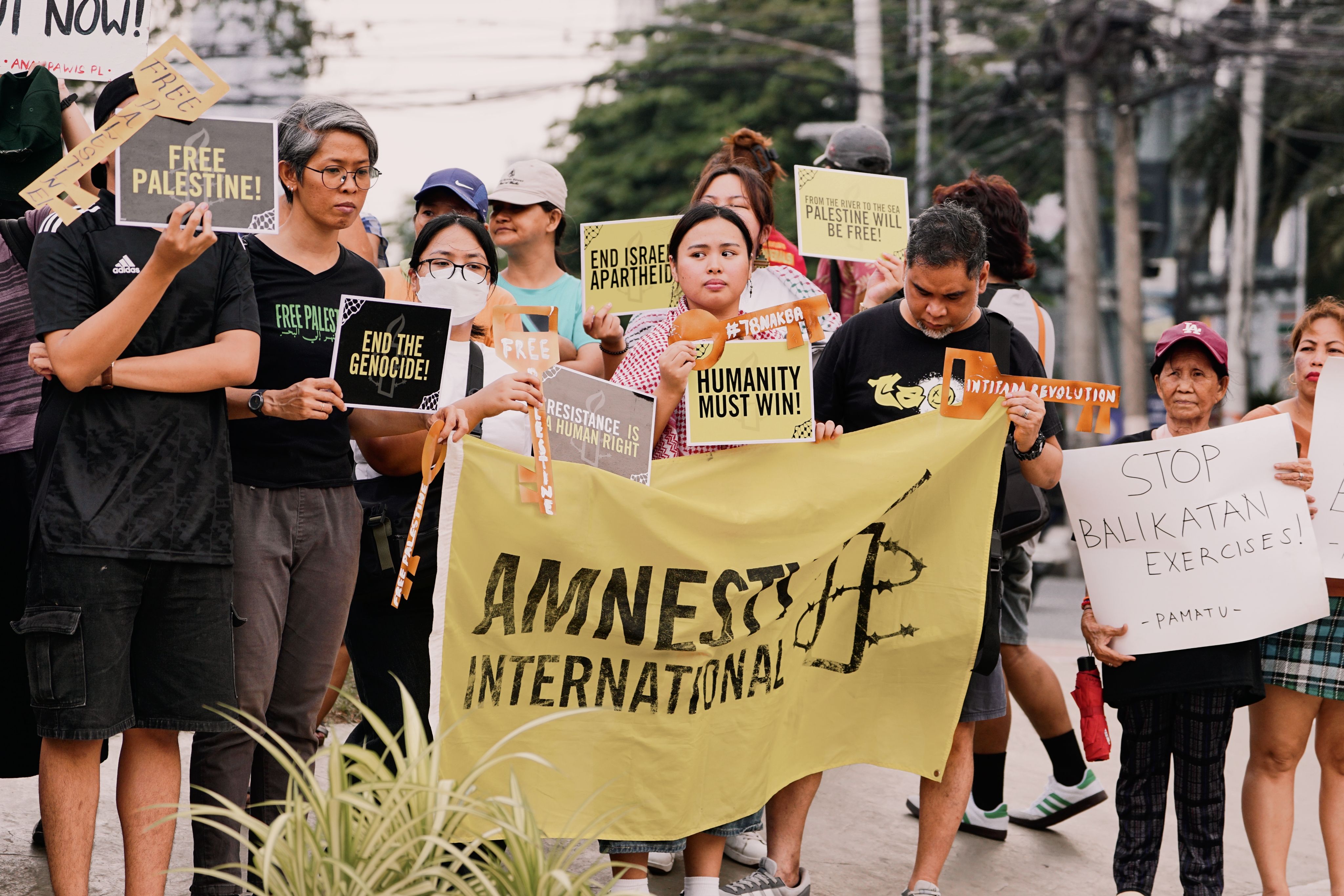 A group of protesters hold signs advocating human rights and justice in an outdoor rally.