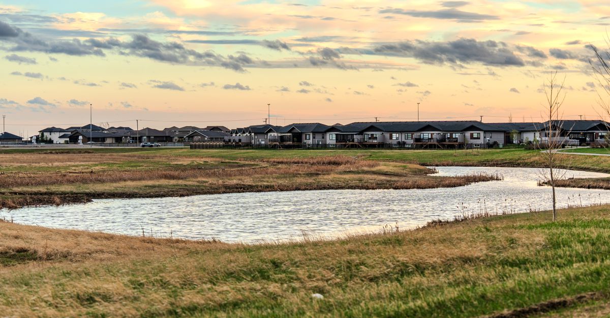 A serene suburban scene with a pond and houses under a colorful sunset sky.