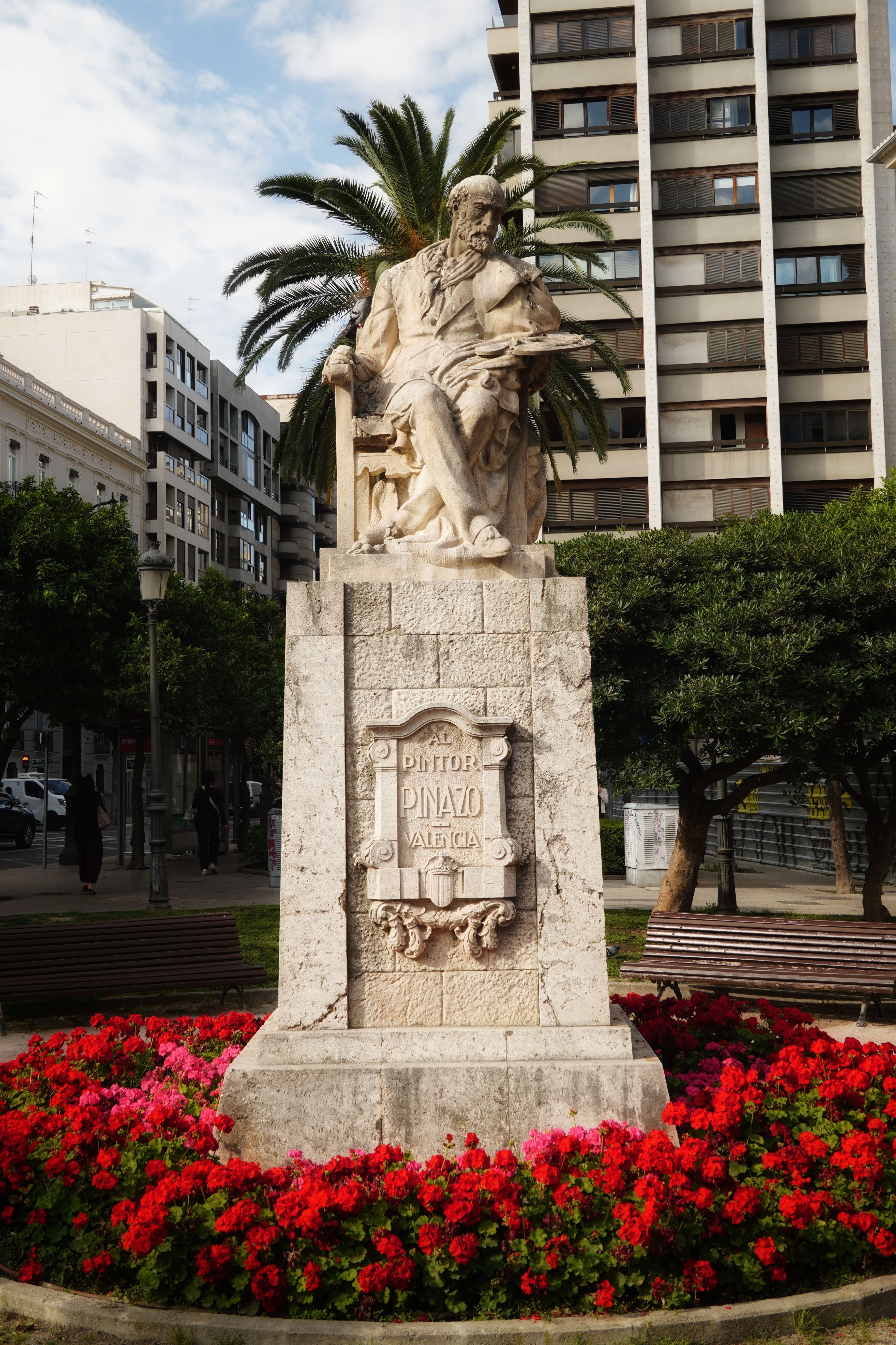 Dramatic statue surrounded by vibrant flowers in a city park, showcasing urban and artistic appeal.