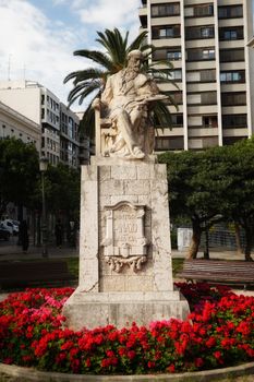 Dramatic statue surrounded by vibrant flowers in a city park, showcasing urban and artistic appeal.