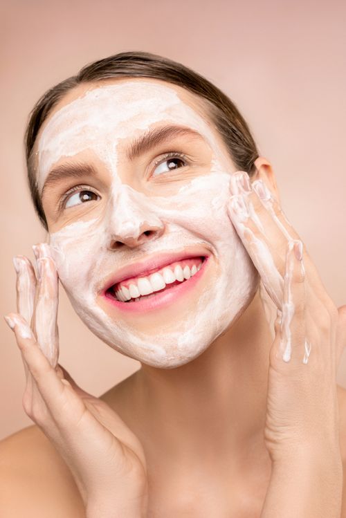 Free Smiling woman applying facial foam during skincare routine, showcasing joy and care. Stock Photo