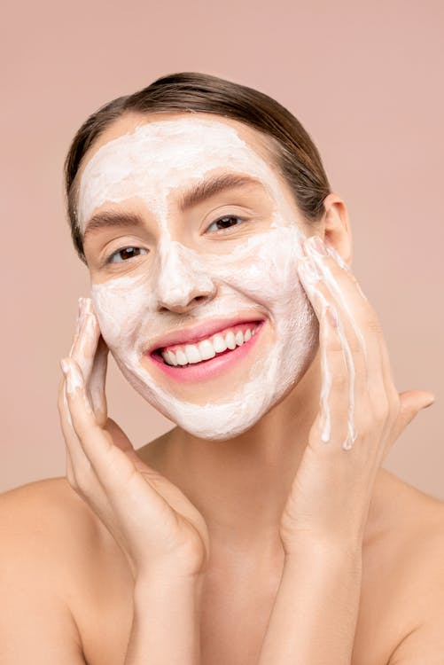 Free Woman with a radiant smile applying facial foam cleanser, promoting skincare routine. Stock Photo