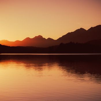 Dramatic sunset reflecting on Nahuel Huapi Lake with Andes mountains silhouette, Bariloche, Argentina.