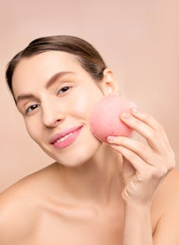 Young woman enjoying skincare with a pink makeup sponge, showcasing a bright smile.