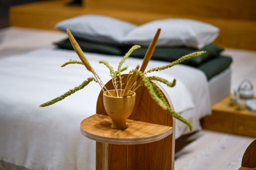A cozy, minimalist bedroom with dried plants in a vase, featuring neutral tones and warm aesthetics.