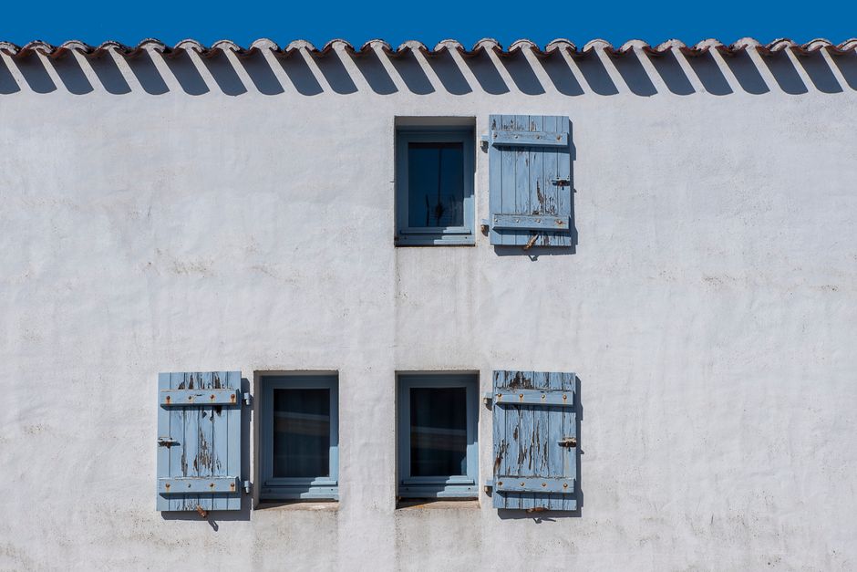 Weathered Mediterranean rendered wall with aged blue shutters showing coastal exposure and surface wear