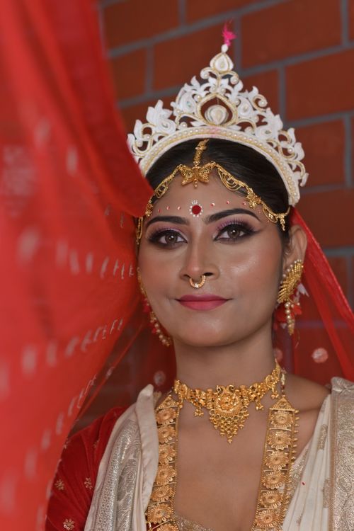 Free Close-up portrait of a traditional Bengali bride wearing red saree and gold jewelry indoors. Stock Photo