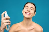 一位快乐的女士闭着眼睛，在蓝色背景下喷洒面部薄雾，展现护肤与幸福