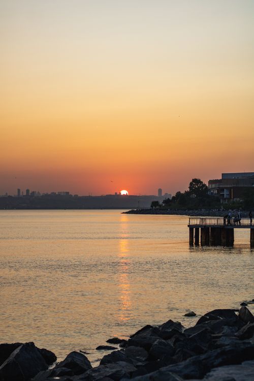 Free Beautiful sunset over a tranquil lake with a scenic pier and rocky shore. Stock Photo