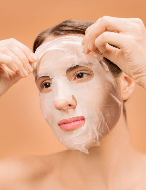 Free Close-up of a woman applying a facial sheet mask for skincare on a neutral background. Stock Photo