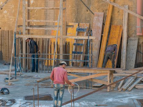 Three construction workers on an outdoor building site surrounded by wooden planks and metal rods.