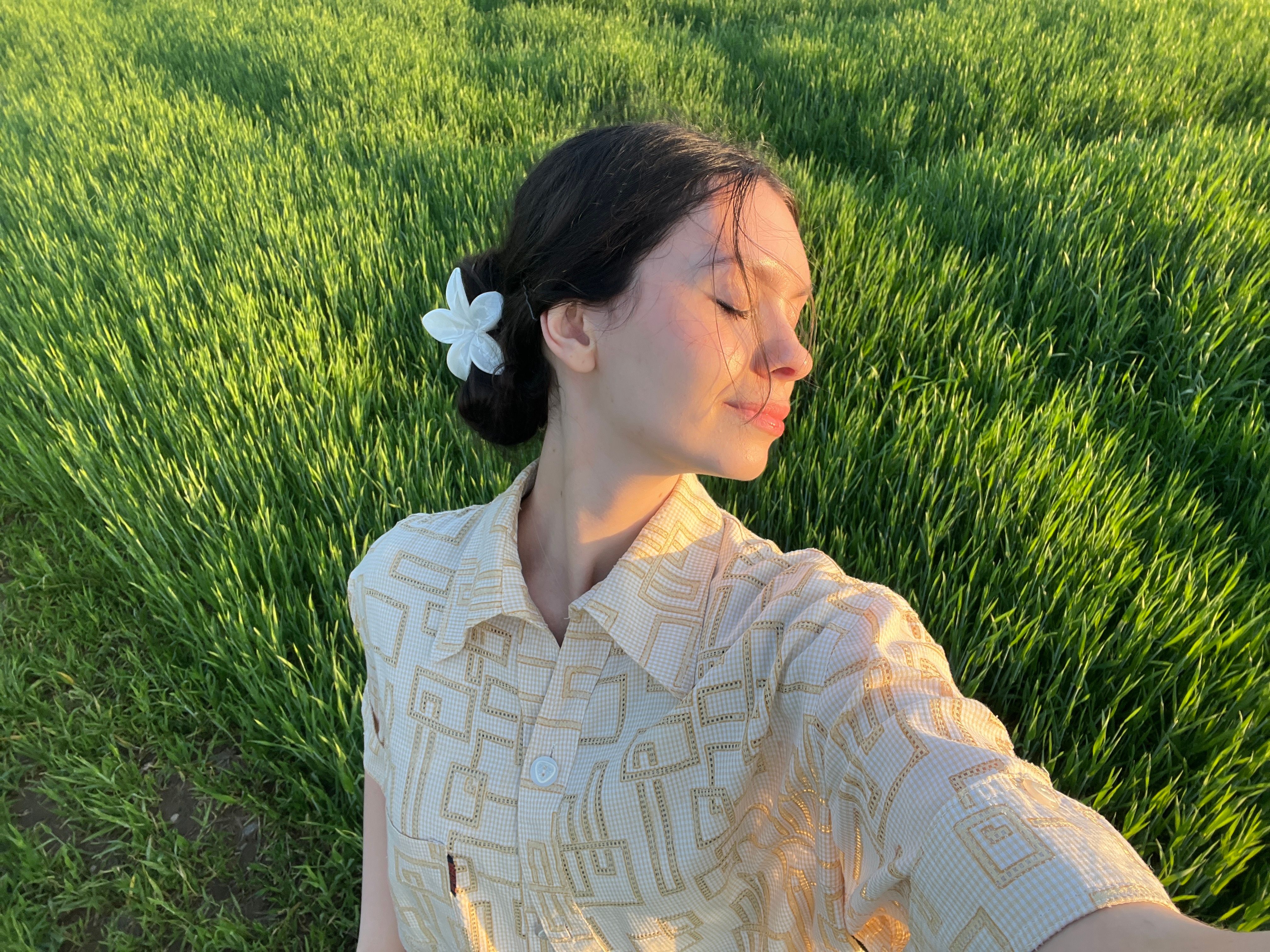 A woman with a flower in her hair basks in the golden sunlight amidst vibrant green grass.