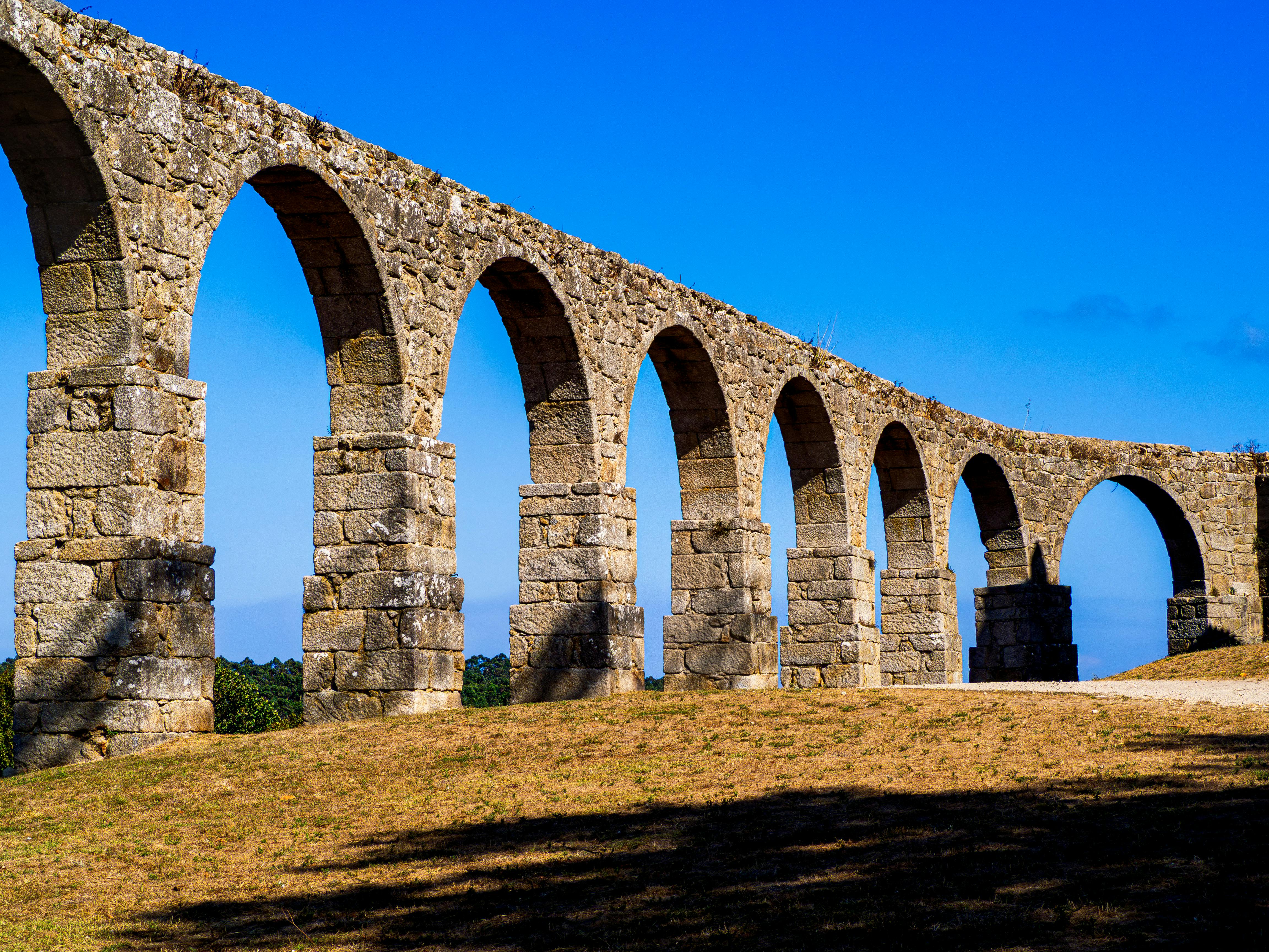 Stone arches of the historic aqueduct in Vila do Conde under a clear blue sky.