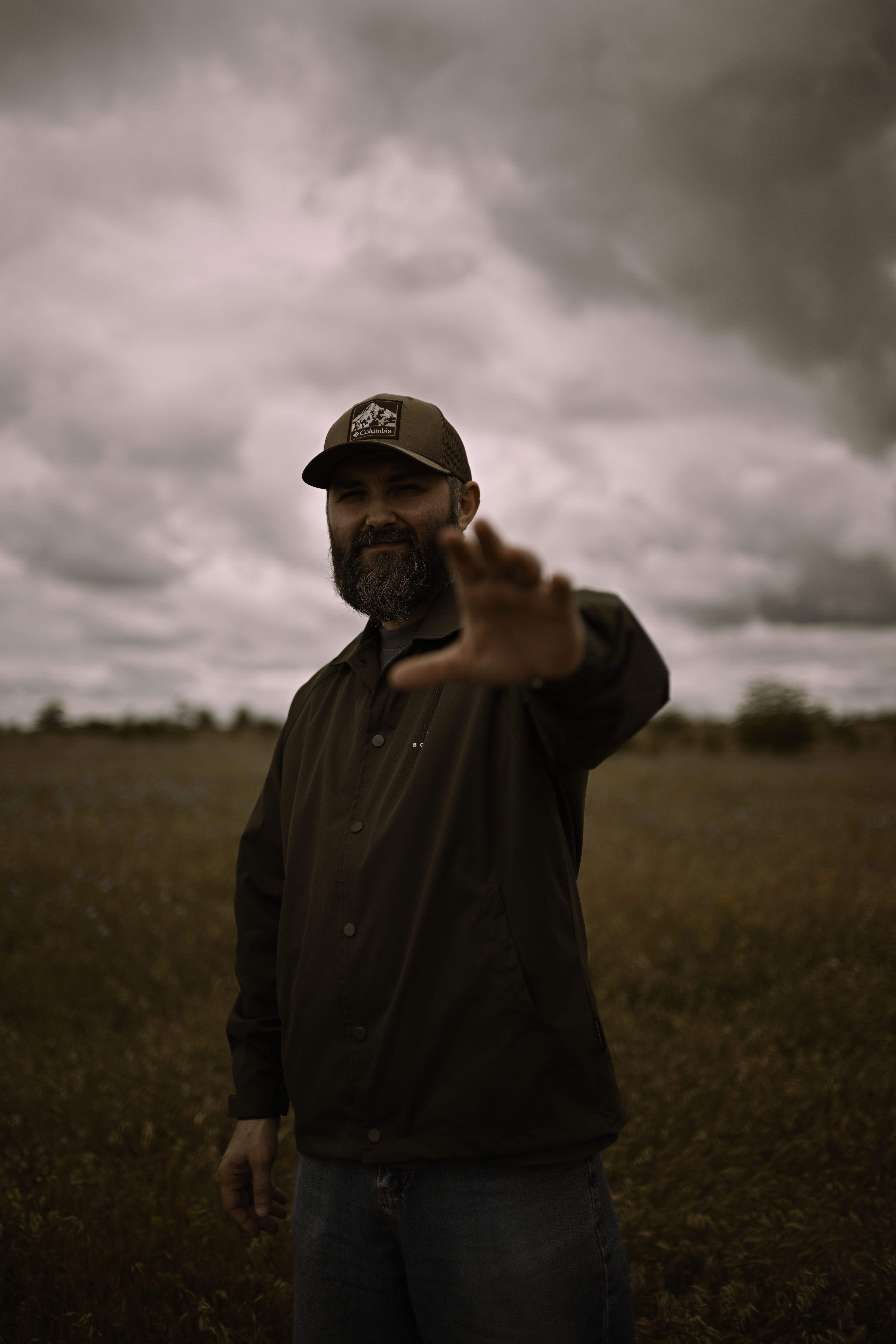 Bearded man reaching out in a field under cloudy skies · Free Stock Photo