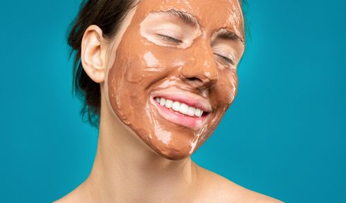 Free Close-up of a woman smiling with a clay mud face mask, emphasizing skincare and relaxation. Stock Photo