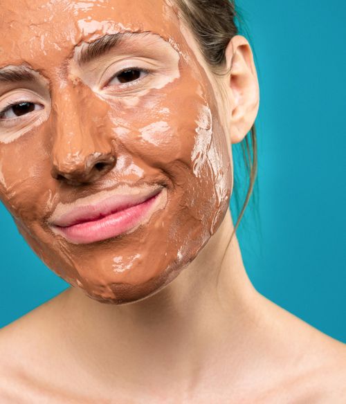 Free Close-up of a smiling woman wearing a clay face mask against a blue background. Stock Photo