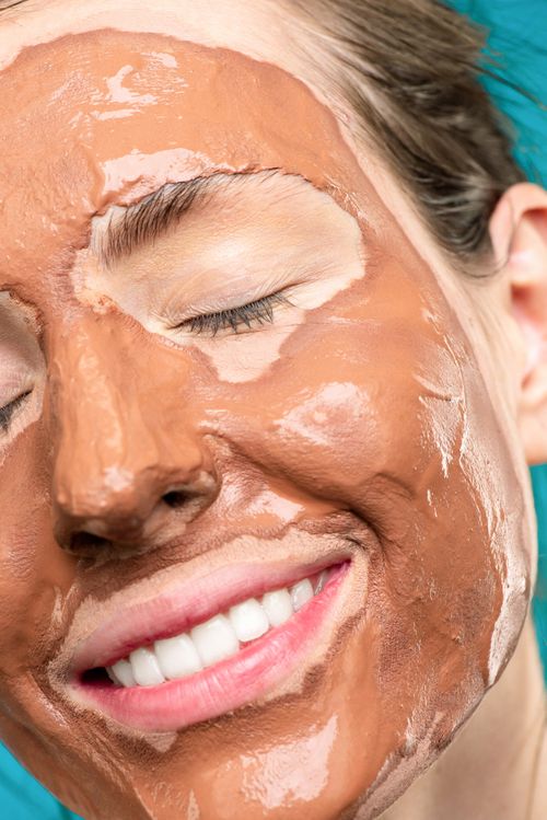 Free Close-up of a woman smiling with a brown clay face mask for skincare and relaxation. Stock Photo
