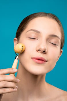 Close-up of a woman applying facial roller for skincare on a blue background.