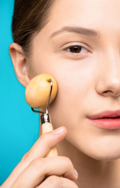Free Close-up of a woman using a facial roller on her cheek for radiant skin care treatment. Stock Photo