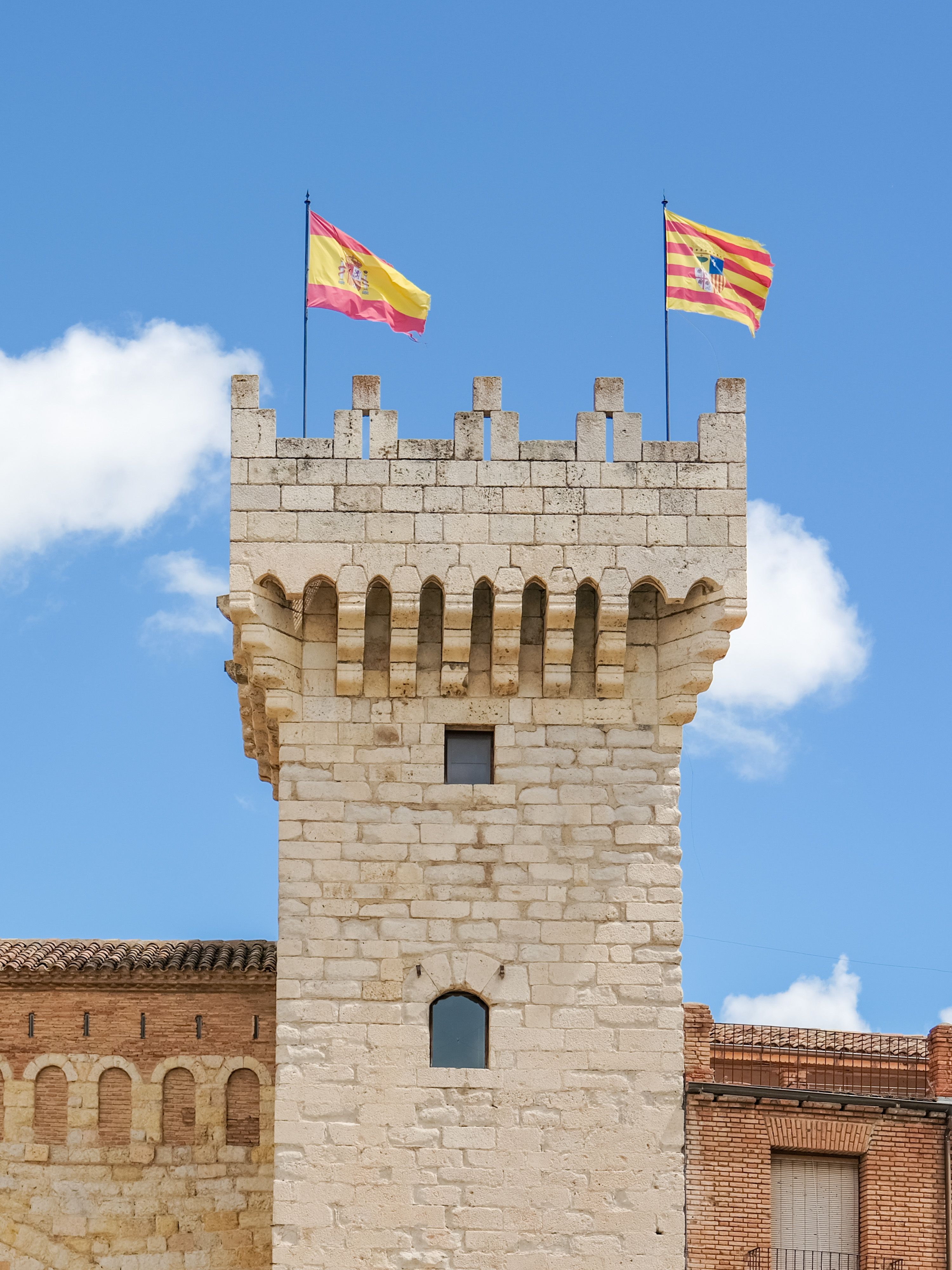 Stone tower in Daroca, Spain, adorned with Spanish and Aragon flags under a clear blue sky.