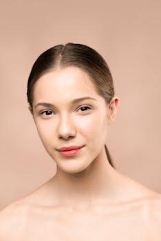 A woman with a radiant smile and flawless skin stands against a beige background.
