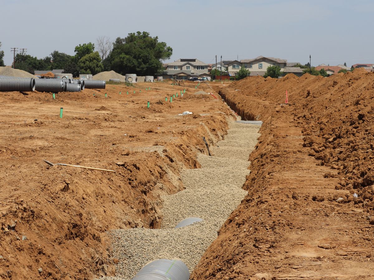 Wide view of a construction site with trenches and large pipes in a suburban area