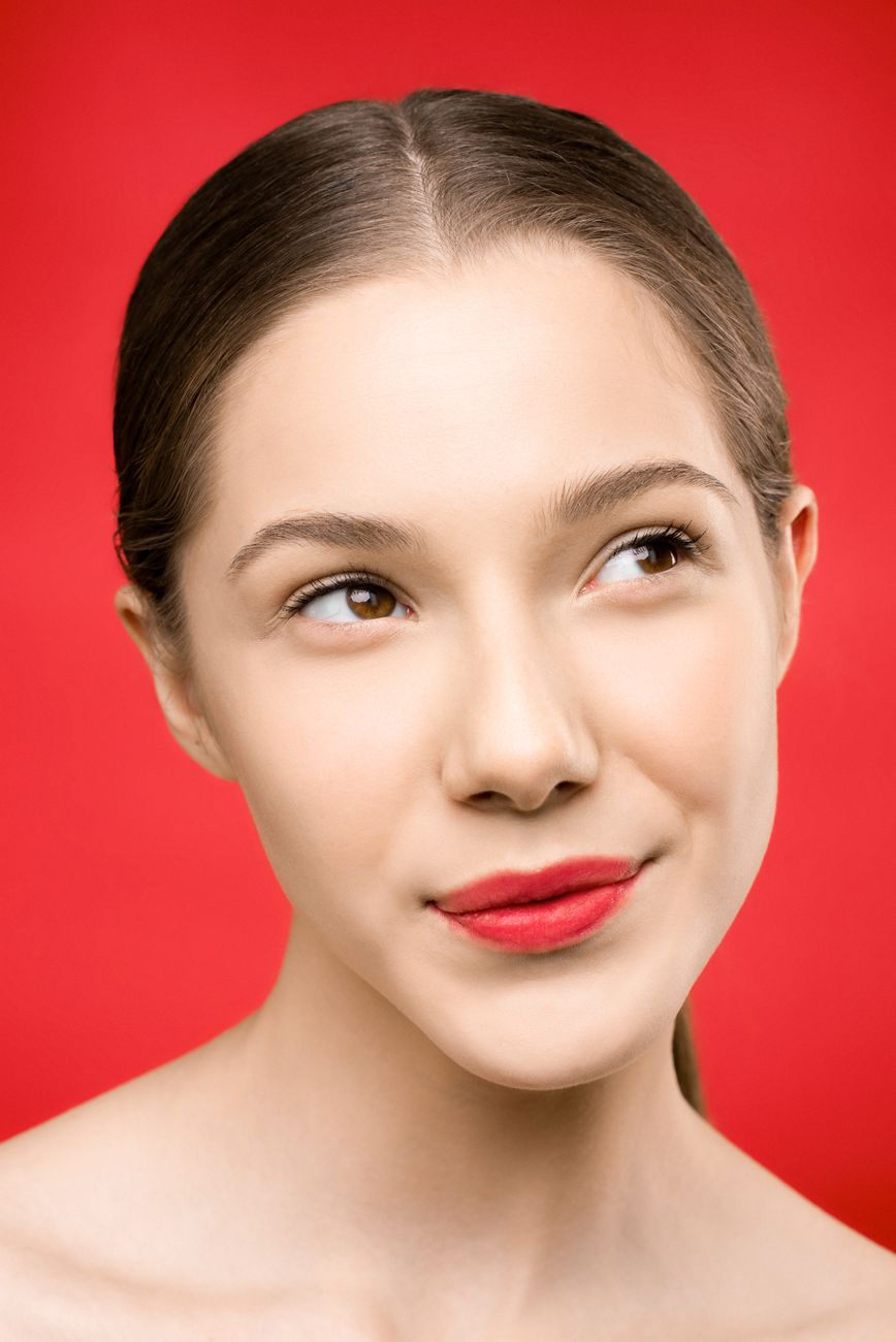 Elegant portrait of a young woman with red lipstick against a vibrant red background.