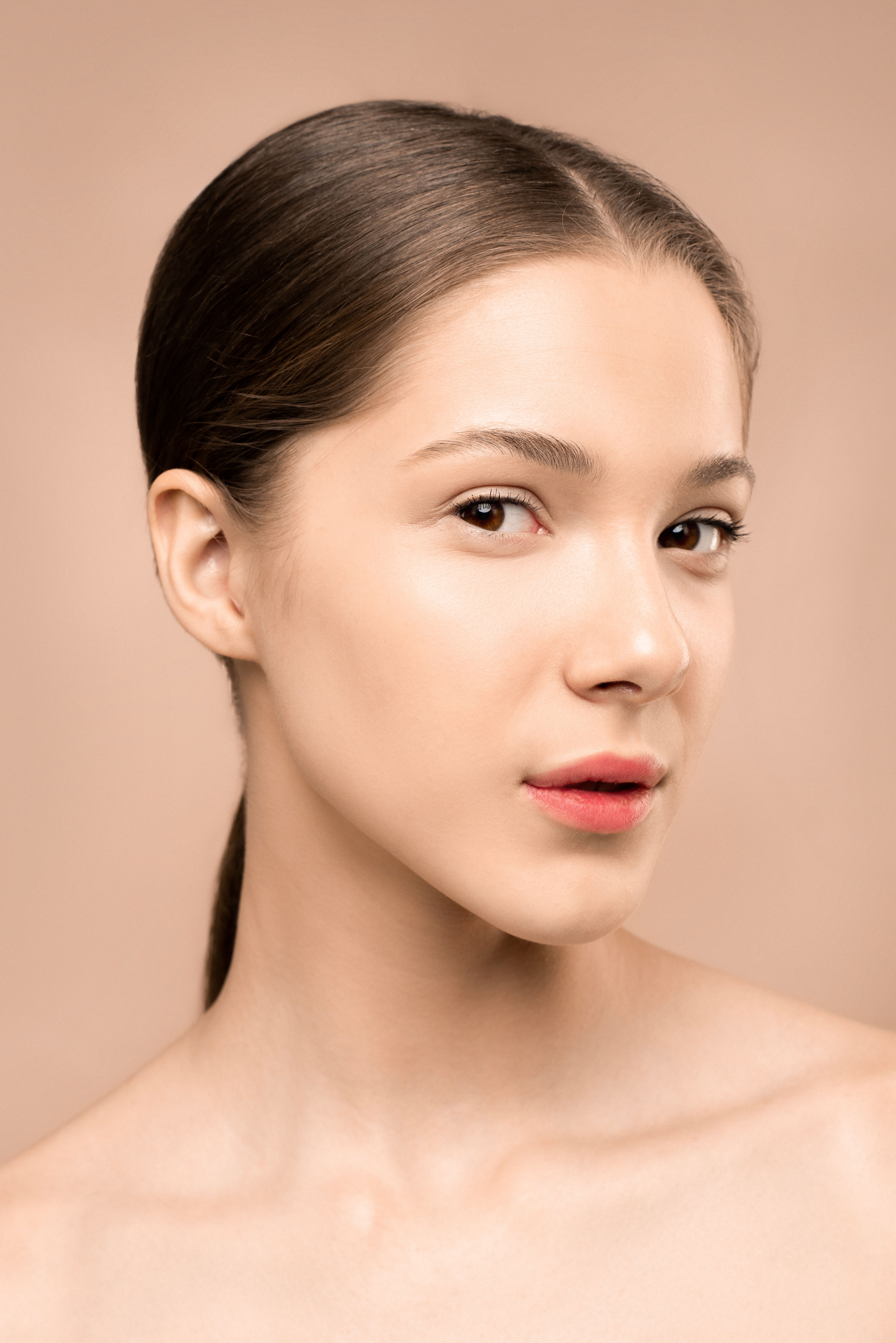 Close-up portrait of a young woman against a beige background, showcasing elegance and beauty.