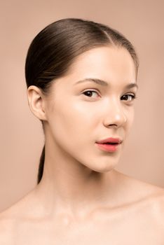 Close-up portrait of a young woman against a beige background, showcasing elegance and beauty.