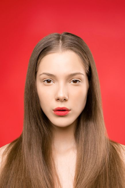A captivating portrait of a young woman with long hair and red lipstick against a vibrant red background.
