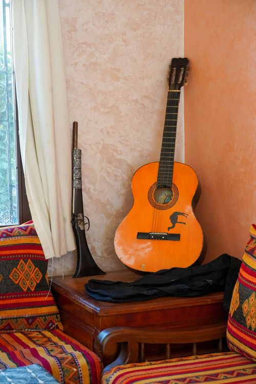 Free A cozy corner with a guitar, vintage rifle, and colorful cushions, exuding a rustic charm. Stock Photo