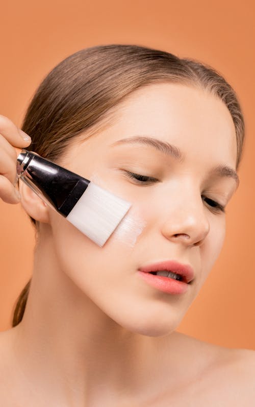 Frau, Die Feuchtigkeitscreme Auf Ihrem Gesicht Unter Verwendung Des Pinsels Anwendet