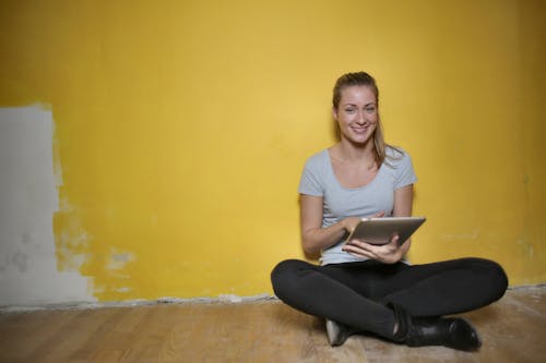 бесплатная Женщина, сидящая на деревянном полу с помощью планшета Стоковое фото