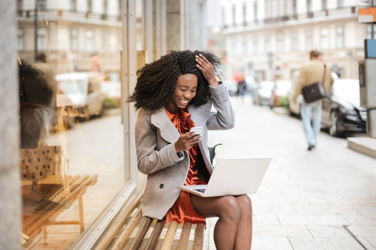 Woman in an orange dress using a laptop and smartphone outdoors