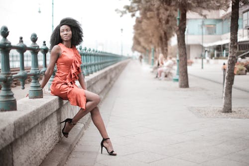 Selective Focus Photo of Woman in Orange Dress Sitting on Concrete Block